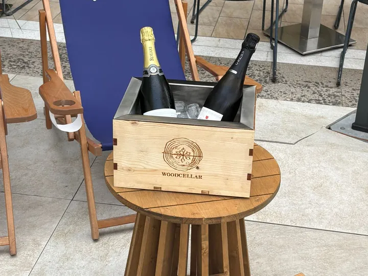 Glacetta Wood Cellar in abete con due bottiglie di spumante nel ghiaccio, su un tavolino di legno tra le sdraio di un dehors.